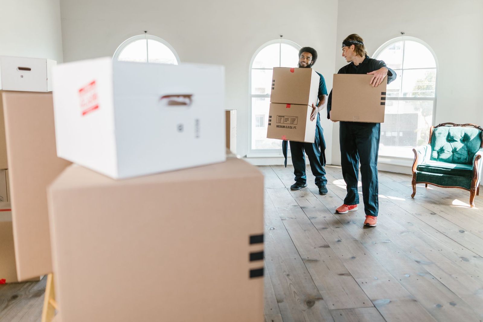 Zwei Umzugshelfer in Arbeitskleidung tragen Kartons in eine helle Wohnung